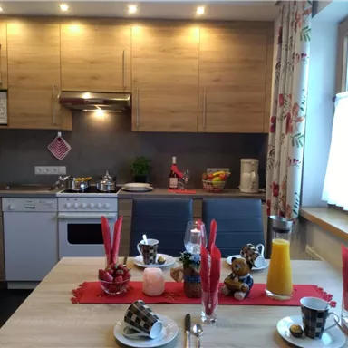 Eine gemütliche Küche mit modernen Geräten und einem Esstisch, der festlich gedeckt ist. Auf dem Tisch stehen Getränke, Süßigkeiten und Dekorationen, die eine einladende Atmosphäre schaffen.