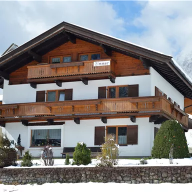 Ein schönes alpenländisches Haus mit Holzbalkonen. Schnee bedeckt den Garten und die Umgebung.