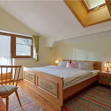 Ein gemütliches Schlafzimmer mit einem großen Bett, einem Tisch und einem Stuhl. Das Zimmer hat Fenster mit Vorhängen und einen warmen, einladenden Farbton.