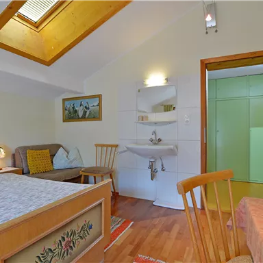 Ein gemütliches Zimmer mit einem Doppelbett, Stühlen und einem Waschbecken. Ein helles Fenster sorgt für Tageslicht.