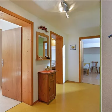 Ein heller Flur mit Holzdetails und mehreren Türen. Eine kleine Kommode und ein Spiegel ergänzen die Einrichtung.