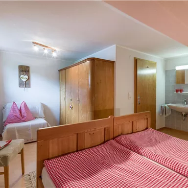 Ein gemütliches Schlafzimmer mit zwei Einzelbetten, einem Holzschrank und einem kleinen Waschbecken. Die Wände sind hell und das Zimmer ist gut beleuchtet.