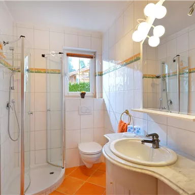 A modern bathroom with a shower, a sink, and a white toilet. Orange towels and bright lighting create a friendly atmosphere.