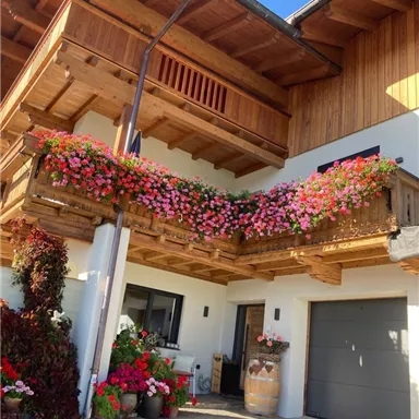 Ein schönes Haus mit einem Holz-Balkon, der mit bunten Blumen geschmückt ist. Der Eingangsbereich ist ebenfalls blumig dekoriert und es gibt eine Garage.