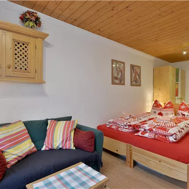 Ein gemütliches Zimmer mit einem Doppelbett und dekorativen Kissen. Eine Sitzecke mit farbigen Kissen und einem kleinen Tisch rundet das Ambiente ab.