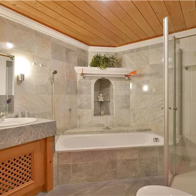 Ein modernes Badezimmer mit einer Badewanne und einer Dusche. Die Wände sind mit grauem Marmor gefliest, und Holzdetails verleihen dem Raum eine warme Atmosphäre.