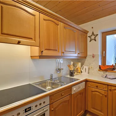 Eine moderne Küche mit Holzschränken und einem hellen Innenraum. Sie ist gut ausgestattet mit einem Herd, Spüle und Fenster.