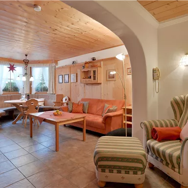 Ein gemütliches Wohnzimmer mit Holzmöbeln und einer hellen, einladenden Atmosphäre. Es gibt einen Esstisch, ein Sofa und einen bequemen Sessel.