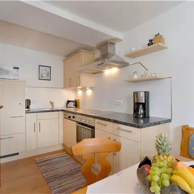 A modern kitchen with bright cabinets and a dining area. Fresh fruit is on the table and there is a cozy atmosphere.