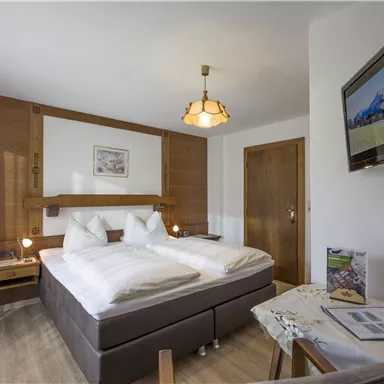 A cozy double room with two beds and bright furnishings. A television and a small table are also available.