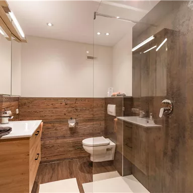 Ein modernes Badezimmer mit Holzverkleidung und einer großen Duschkabine. Es verfügt über eine stilvolle Waschbeckenanordnung und viel natürliches Licht.