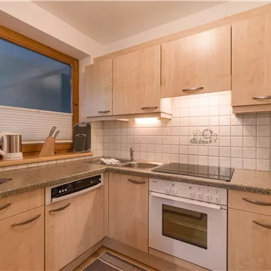 Eine moderne Küche mit Holzschränken und einer hellen Arbeitsfläche. Neben einem Fenster sind Kochgeräte und eine Kaffeemaschine auf der Arbeitsplatte platziert.