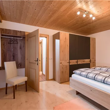 Ein schlichtes Schlafzimmer mit einem Holzfußboden und einer Decke aus Holzpaneelen. Es gibt ein Bett mit einer karierten Bettdecke und eine Garderobe.
