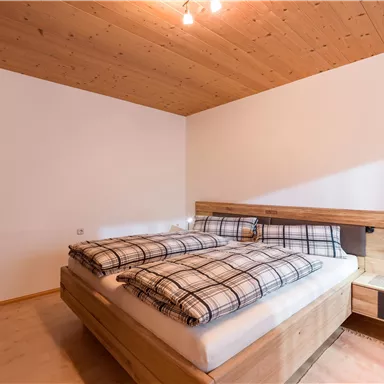 Ein modernes Schlafzimmer mit einem großen Doppelbett und einem Holzdekor. Die Wände sind hell, und es gibt eine angenehme Beleuchtung.