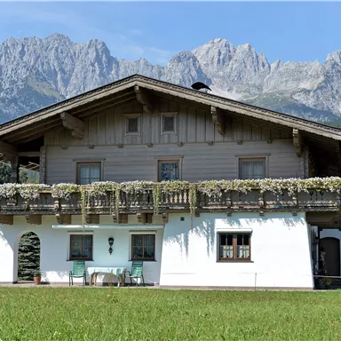 Ein traditionelles Alpenhaus mit einem Balkon und einem schönen Garten. Im Hintergrund sind die majestätischen Berge sichtbar.