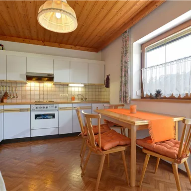 Eine helle Küche mit Holzdecke und modernen Geräten. Der Essbereich ist mit einem Tisch und Stühlen in warmen Farben ausgestattet.