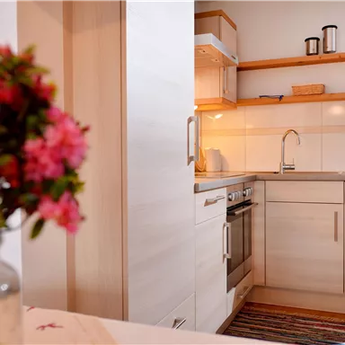 Eine helle und moderne Küche mit Schränken und Geräten in neutralen Farben. Im Vordergrund steht eine Vase mit bunten Blumen.