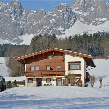 Ein charmantes Haus inmitten einer schneebedeckten Landschaft. Im Hintergrund erheben sich majestätische Berge.