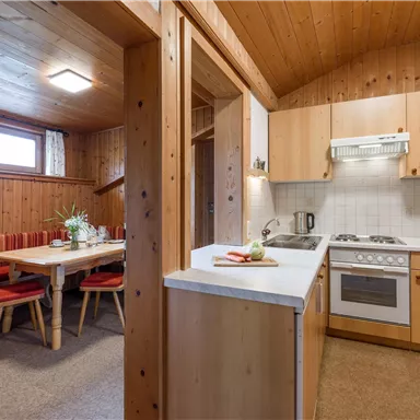 Eine gemütliche Küche mit Holzverkleidung und einem Esstisch. Die Ausstattung umfasst einen Herd und eine Spüle, verbunden mit einem angrenzenden Wohnbereich.