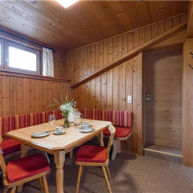 Ein gemütlicher Raum mit Holzwänden und roten Polstern. Ein Esstisch ist gedeckt und eine Treppe führt zu einem anderen Bereich.