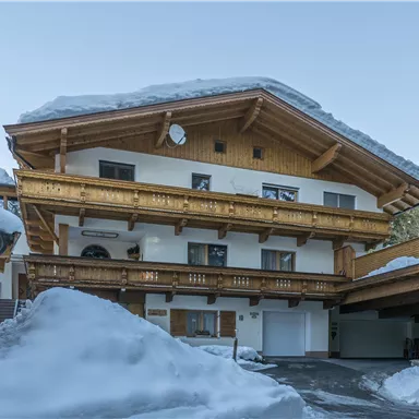 A charming building in alpine style, surrounded by snow. The wooden balconies and the design give the house a cozy atmosphere.