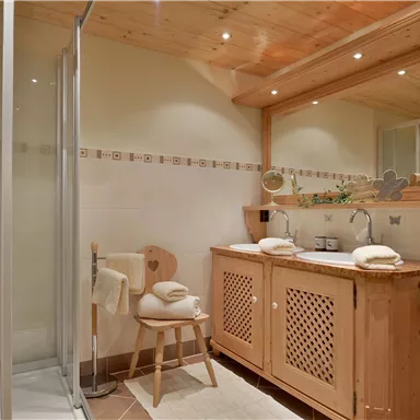 A modern bathroom with a glass shower and a wooden washbasin. Fresh towels are placed on the table and a mirror is mounted on the wall.