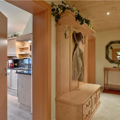 An inviting hallway with wood paneling and a wardrobe. On the left side, an open kitchen is visible.