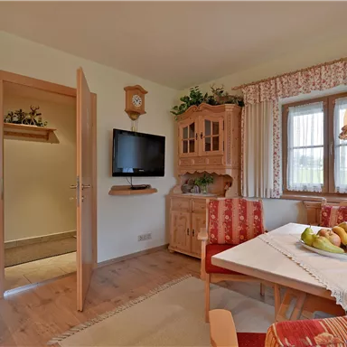 A cozy kitchen with a dining table and chairs. A lamp hangs above the table, and a TV is mounted on the wall.