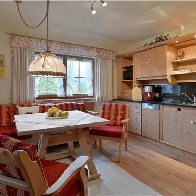A cozy kitchen with wooden furniture and a large dining table. The warm colors and bright light create an inviting atmosphere.