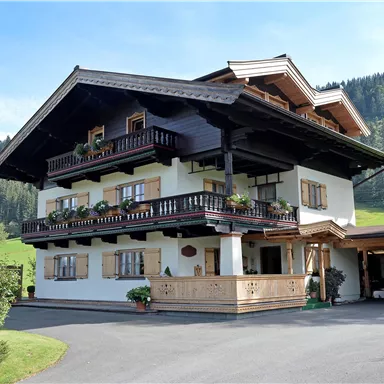 A traditional old wooden house with balconies and flower boxes. Surrounded by green meadows and mountains.