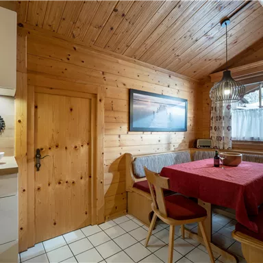 Eine gemütliche Holzstube mit einem roten Tisch und Sitzbänken. Die Atmosphäre ist warm und einladend, ideal für gesellige Zusammenkünfte.