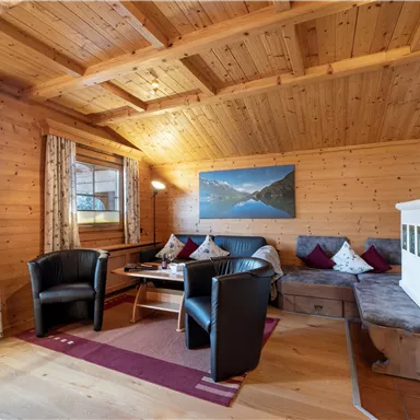 Ein gemütlicher Wohnraum mit Holzverkleidung und einem großen Fenster. Es gibt bequeme Sitzgelegenheiten und einen Tisch in einer warmen Atmosphäre.