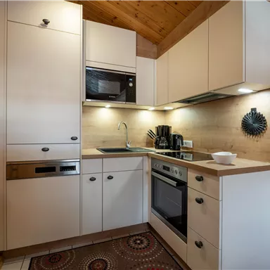 Eine moderne Küche mit weißen Schränken und Holzakzenten. Sie ist kompakt und gut ausgestattet mit verschiedenen Geräten.