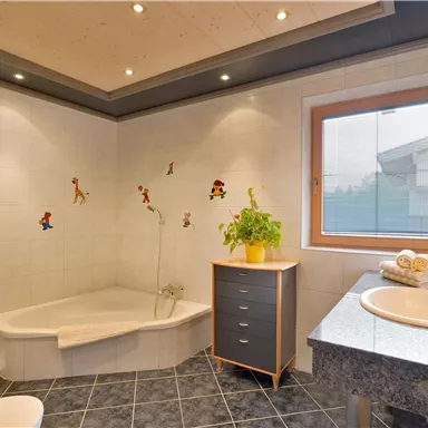 Ein modernes Badezimmer mit einer Badewanne und einer Dusche. Es gibt eine Pflanze und farbenfrohe Wandaufkleber für Kinder.