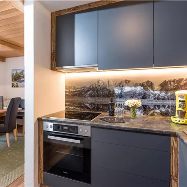 Eine moderne Küche mit eleganten, dunklen Schränken und einer schönen Arbeitsplatte. Im Hintergrund ist eine stilvolle Berglandschaft zu sehen, während eine gelbe Kaffeemaschine den Raum akzentuiert.