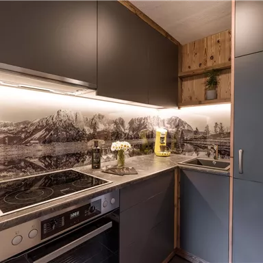 Eine moderne Küche mit eleganten grauen Schränken und einer stilvollen Arbeitsplatte. Im Hintergrund ist eine malerische Berglandschaft zu sehen.