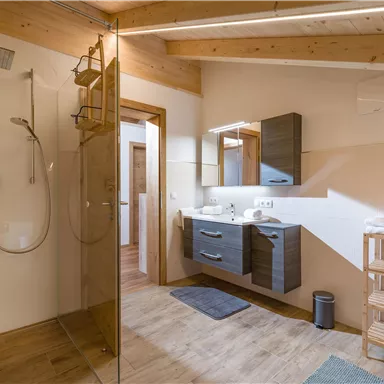 A modern bathroom with a glass shower and a wooden sink. The walls are light, and there is a relaxed atmosphere.