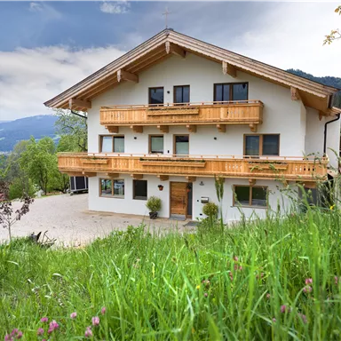 A modern house in alpine style with wooden balustrades and spacious balconies. Surrounded by green meadows and mountainous landscape.