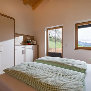 A cozy bedroom with two single beds and green checked duvet covers. There is a beautiful view of the landscape through the window.