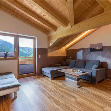 A modern living room with a wooden ceiling and large windows. It is bright and friendly, with a cozy couch and a table.