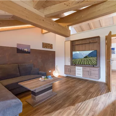 A modern living room with a cozy couch and a television on the wall. The room features a wooden ceiling and floor as well as a harmonious color scheme.