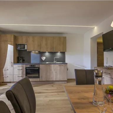 A modern kitchen with wooden cabinets and a dining table. The space is bright and inviting with plenty of natural light.