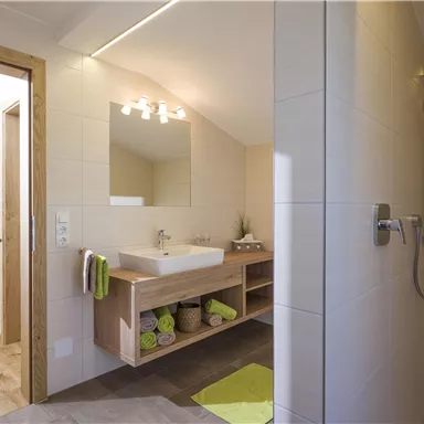 A modern bathroom with a shower and a sink. There are bright tiles and subtle decorative elements.