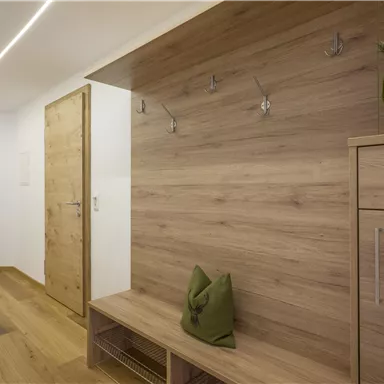 A modern entrance area with wooden walls and a simple seating area. Coat hooks for jackets and coats are hanging on the wall.