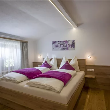 A modern bedroom with a double bed and purple pillows. Bright walls and wooden furniture create a cozy atmosphere.