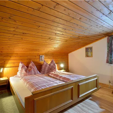 Ein gemütliches Schlafzimmer im Dachgeschoss mit zwei Holzbetten und karierten Bettwäsche. Die Holzvertäfelung und das Fenster sorgen für eine warme Atmosphäre.