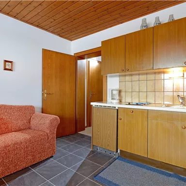 Eine gemütliche Küche mit einer roten Couch und Holzmöbeln. Der Raum hat eine helle Atmosphäre und einen modernen Touch.