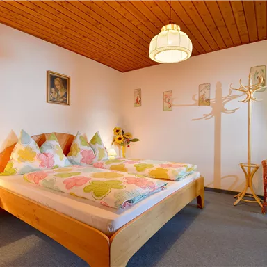 Ein einladendes Schlafzimmer mit einem großen Bett und bunten Bettdecken. Eine gemütliche Sitzecke und eine Lampe schaffen eine warme Atmosphäre.
