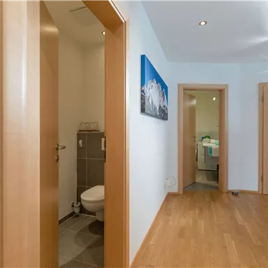 Ein helles Flur mit Holzfußboden und mehreren Türen. An der Wand hängt ein Bild mit einem Bergmotiv.