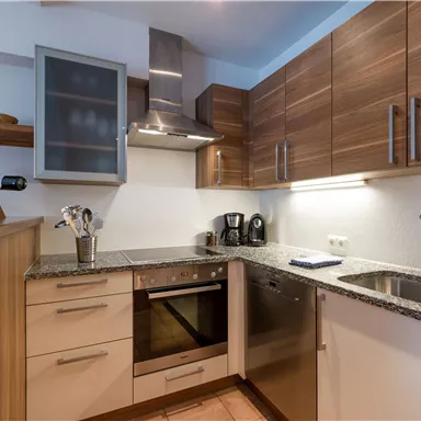 Eine moderne Küche mit Holzschränken und einer Arbeitsfläche aus Granit. Sie ist mit Elektrogeräten wie einem Herd und einer Spülmaschine ausgestattet.